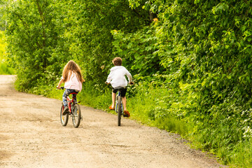Fototapeta premium Two children ride nearby on bicycles in the park on a summer sunny day.