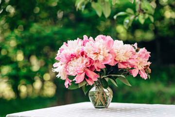 Bouquet of pink romantic peonies flowers in a glass vase on a table in the summer outdoors. Soft selective focus bokeh.