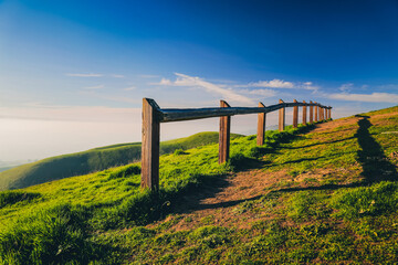 Obraz premium Observation point with wooden fence in green hills at sunset