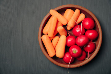 Radishes and carrots on a plate on a dark background top view