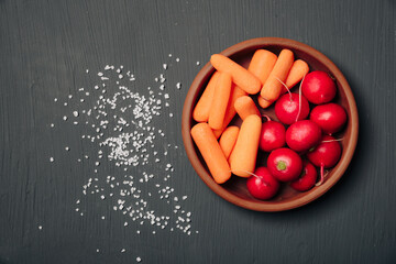 Radishes and carrots on a plate on a dark background top view