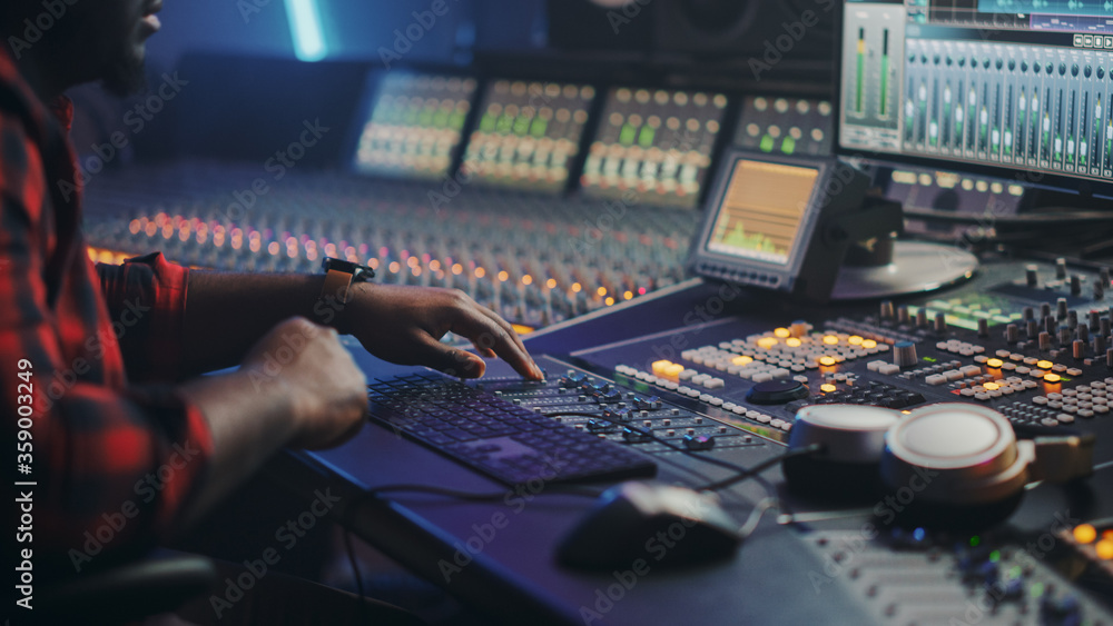 Poster energetic male audio engineer / producer working in music recording studio, mixing tracks on control