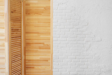 Louvered wooden screen on a white brick wall background with copy space.
