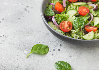 Healthy fresh vegetables salad with cucumbers and tomatoes, red onion and spinach in grey bowl on dark background