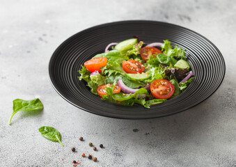 Healthy fresh vegetables salad with cucumbers and tomatoes, red onion and spinach in black bowl on dark background