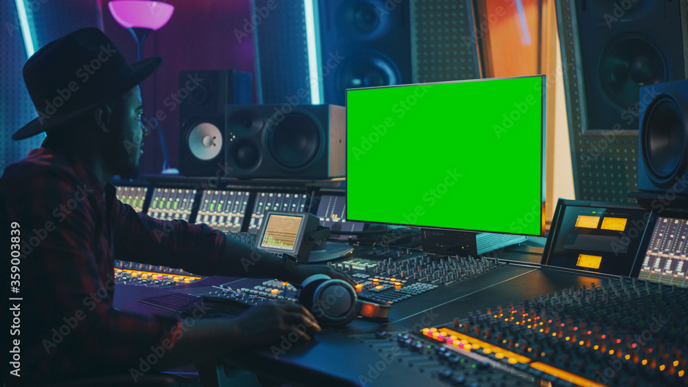 Fototapete Stylish Audio Producer Working in Music Record Studio, Uses Green Screen Chroma key Computer Display, Mixer Board Equalizer and Control Desk to Create New Hit Song. Creative Black Artist Musician