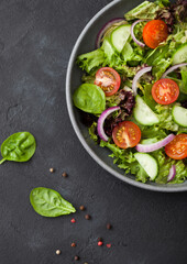 Fresh healthy vegetarian vegetables salad with tomatoes and cucumber, red onion and spinach in large grey bowl plate on dark background.