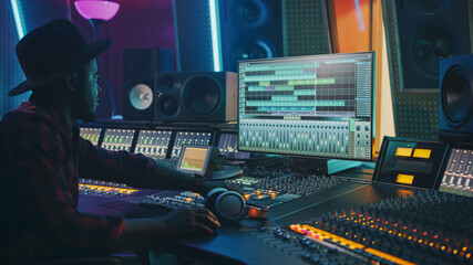 Stylish Audio Engineer Working in Music Recording Studio, Uses Mixing Board and Software to Create...