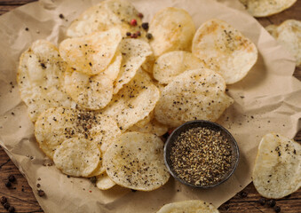 Potato crisps chips with black pepper taste on paper with ground pepper on wood table background.