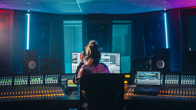 Stylish Artist, Musician, Audio Engineer, Producer Takes Place at His Control Desk in Music Record Studio, Uses Computer Screen show User Interface of DAW Software with Song Playing. Back View