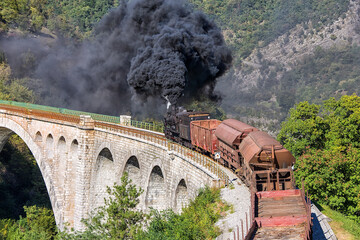 Obraz premium Old steam train crossing the Solkan bridge in Nova Gorica, Slovenia, Europe. Lots of black and gray steam hiding the locomotive, full frame.
