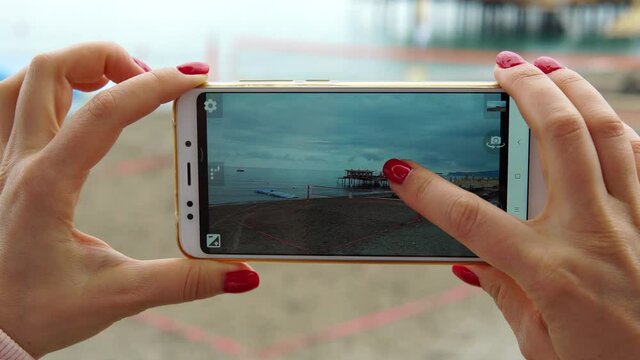 Woman tourist photographs with smartphone evening sea and pier at a resort in Turkey.