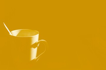 White coffee cup and silver spoon with yellow gold background.