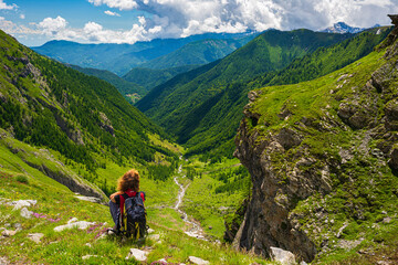 Naklejka na ściany i meble Woman with backpack resting on mountain top, looking at view dramatic landscape valley summer activity fitness wellbeing freedom concept, rear view