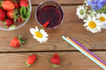 Strawberry compote in a transparent glass on a wooden background with a bouquet of wild flowers, top view