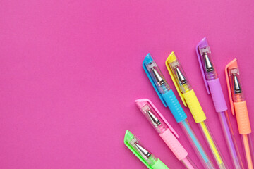 Set of colored pens on pink paper background with copy space