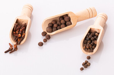 allspice, black pepper and cloves in wooden spoons isolated on a white background