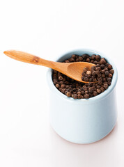 black pepper in a clay pot with a wooden spoon, isolated on a white background
