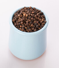 black pepper in a clay pot with a wooden spoon, isolated on a white background