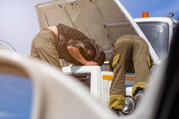 men repairing a truck with manual labor under the open hood with a hand tool, engine accident on a long journey