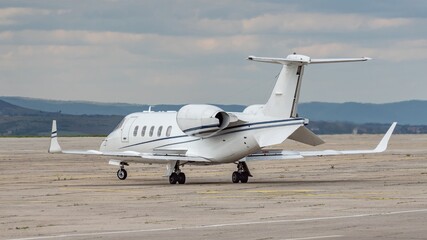 Side view of white small turbofan-powered business jet airplane on the apron of an airport. Cloudy...