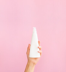 Feminine cosmetic mockup. Plastic pump triangular bottle for a gel or mousse. Feminine hands hold White clean jar. Vertical front view cosmetic banner with copy space. Pink background