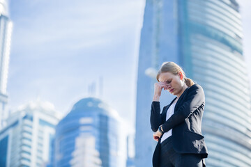 Work stress - Depressed business woman standing with her head down in a modern city with high-rise buildings in the background. 