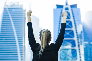 Business success - Passionate young businesswoman celebrating overlooking the city center high-rises with both arms raised.
