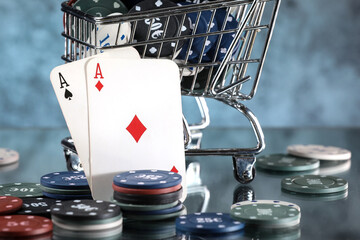 A pair of aces, hearts and diamonds, on a deck of playing cards. Poker playing chips in a blue shopping cart on a dark and light blue background. Online gambling. Addiction. 