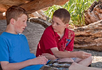 These two Caucasian brothers are talking in their makeshift fort they made at a beach.  One is 13 the other 11 year old boys, waist up, side view horizontal image of family together.