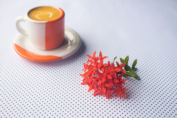 Small bouquet of red flowers next to a cup of orange and white coffee.