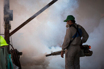 Asian healthcare worker in protective clothing using fogging machine spraying chemical to eliminate...