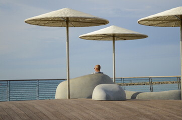 A man is resting in a chillout area on the Tel Aviv beach. Sits under a sun umbrella and looks at the sea.