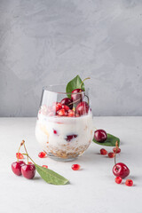 Healthy breakfast in a glass with fresh fruits: pomegranate, cherry, nectarines, honeysuckle, yogurt and granola on a grey background. Shallow depth of field with selective focus
