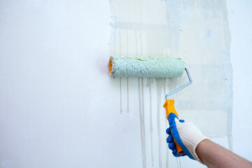 Hand with a paint roller priming the wall before painting
