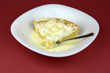 A spoonful of lemon meringue pie and cream served in a white dessert bowl.