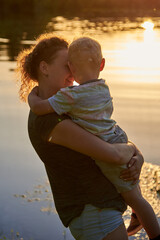 Mom hugs her son on the riverbank at sunset.