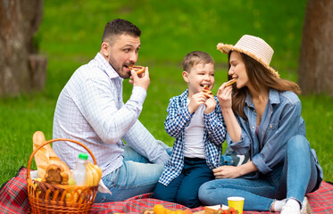 Millennial parents with their son eating pieces of tasty pie on summer picnic in countryside