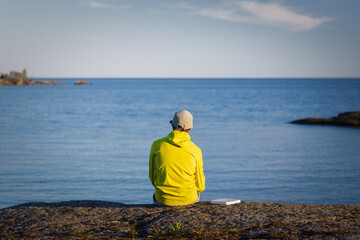 Back view of man sitting on the seashore with a book.