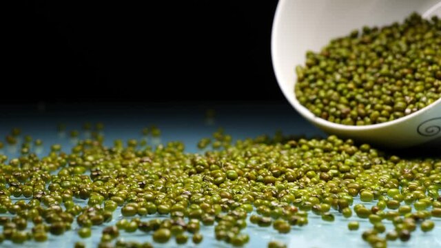 Closeup of mung beans in bowl poured on table, black background, healthy food