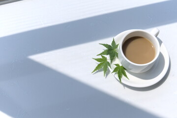 Obraz na płótnie Canvas High-angle shot of cup of milk coffee, three green maple leaves on plate, cup in bright place