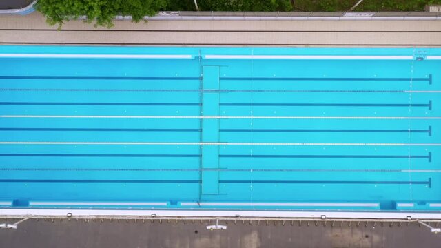 Empty closed swimming pool during quarantine at sports school. Top view zoom out drone shot.