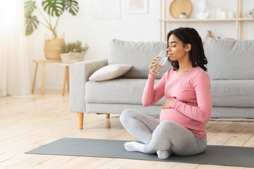 Pregnant woman drinking water during exercising at home