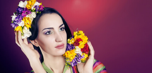 Portrait of a cute girl with bright makeup and with the blooming freesias on his head and hands on a red background in the Studio.