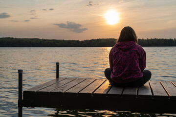 Girl sitting alone on dock facing sunset