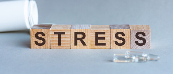 Word STRESS. Stress text on wooden blocks. In front of a row of cubes are ampoules, in the background - white plastic packaging from tablets, the cubes are located on a gray surface. Concept Image.