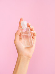 Rose water cosmetic mockup. Female hand holds a transparent jar with a rose water on a pink background. Copy space for your logo branding