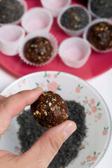 A woman is holding a dried fruit candy in her hand. Balls of prunes, dates and coconut. With a sprinkle of black sesame powder.