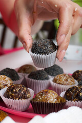 Woman puts dried fruit candies on a plate. Balls of prunes, dates and coconut. With a sprinkle of black sesame powder.