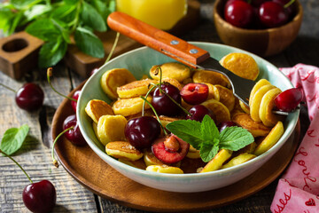 Tiny pancakes trendy food. Mini pancakes with cherries and honey on a rustic wooden table.